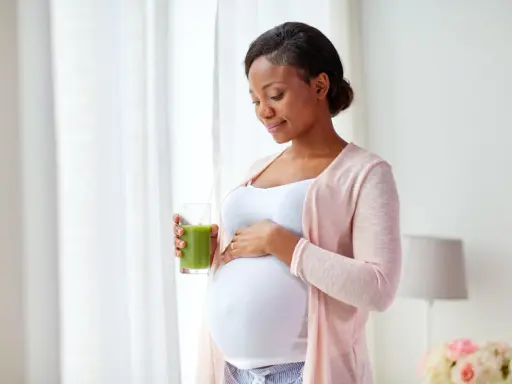 Femme enceinte tenant un verre de jus vert, caressant son ventre. Elle prend soin de sa peau sèche pendant la grossesse.