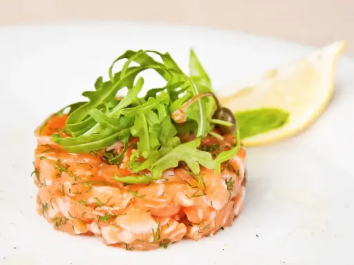 Un délicieux tartare de saumon frais, garni de roquette et d'une tranche de citron, prêt à être dégusté.