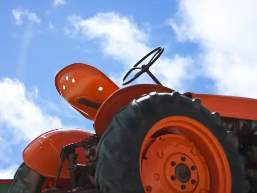 Close-up of an orange tractor's wheel and seat against a blue sky with clouds. This vintage tractor, possibly a different size Kubota tractor, awaits its next task.