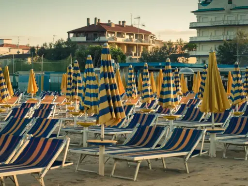 File di sdraio e ombrelloni a righe blu e gialle sulla spiaggia di Cervia Milano Marittima, pronti per accogliere i bagnanti.