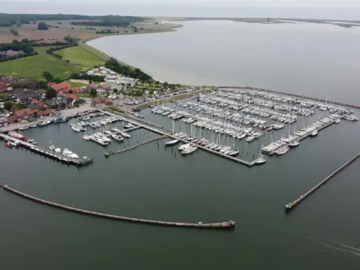 Maasholm Hafen mit vielen Segelbooten und Yachten, die an Stegen liegen. Im Hintergrund ein Dorf und das weite Wasser.
