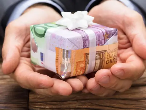 Dłonie trzymają prezent opakowany w banknoty euro. To pomysł, jak zapakować pieniądze na prezent dla dziecka, tworząc unikalną niespodziankę.