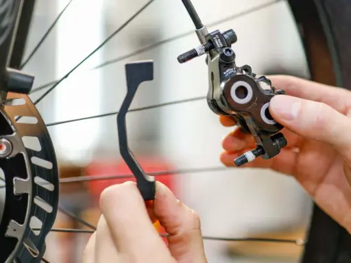 Hände montieren eine Fahrrad-Scheibenbremse. Ein Adapter wird gehalten, um ein Schleifen der Scheibenbremse zu verhindern.