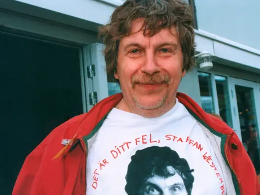 Staffan Westerberg, känd för sina filmer och tv-program, ler i en röd jacka över en t-shirt med hans eget ansikte och texten "Det är ditt fel, Staffan Westerberg".