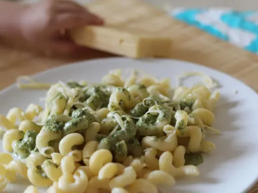 Pyszny makaron ze szpinakiem i parmezanem, gotowy do podania. Dziecko pomaga w przygotowaniu.