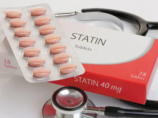 Opakowanie tabletek statynowych i blister z tabletkami. Stetoskop w tle. Statyny na co? Na obniżenie cholesterolu.