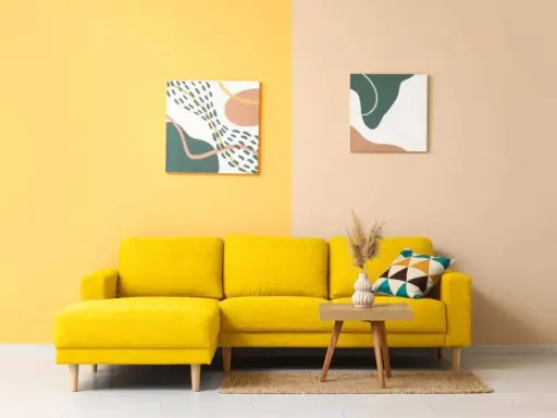 Un divano giallo acceso in una stanza con pareti bicolore. I colori della stanza sono vivaci e moderni, con due quadri astratti che completano l'arredamento.