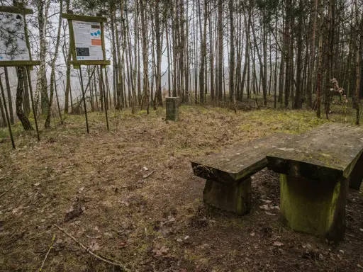 Kamienny stół i ławka w lesie, obok tablice informacyjne. Miejsce na odpoczynek podczas wędrówki po górach obkaskich.