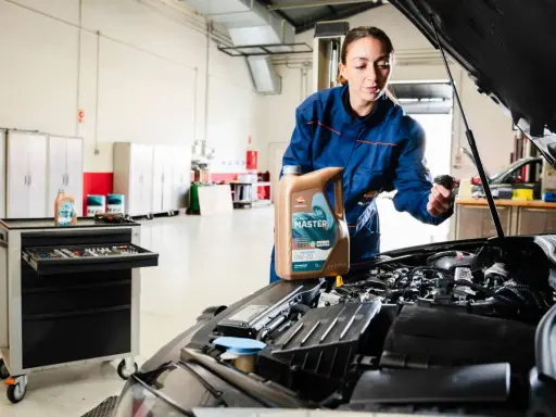 Mecánica muestra cómo cambiar el aceite del coche, sosteniendo una botella de aceite Repsol Master.