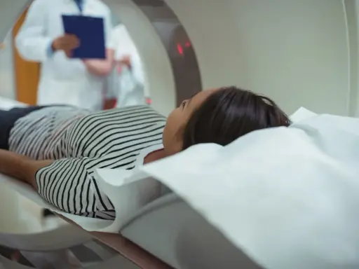 Pacjentka leży na łóżku rezonansu magnetycznego, obok niej stoi lekarz z dokumentacją.