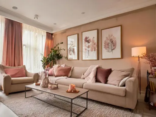 Un salon coloré et chaleureux, avec un canapé beige, des coussins roses et des tableaux de feuilles.