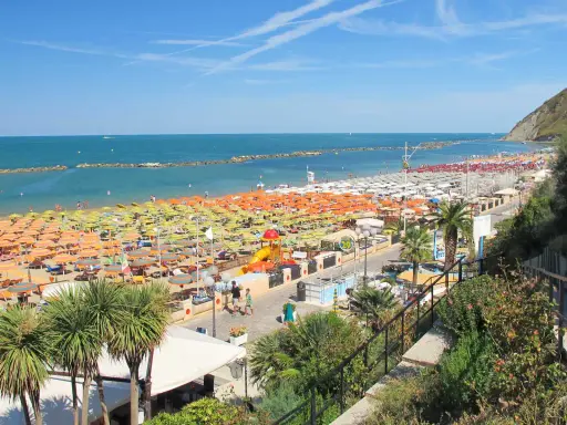 Spiaggia affollata a Gabicce Mare, con file infinite di ombrelloni colorati e lettini. Le recensioni la descrivono come un paradiso estivo.