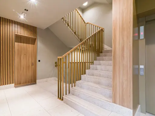 Drewniane lamele i nowoczesna klatka schodowa z metalową balustradą. Idealne inspiracje, co położyć na ściany na klatce schodowej.