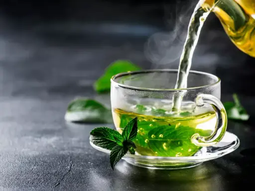 Un thé fumant à la menthe poivrée est versé dans une tasse transparente, ornée d'une feuille de menthe fraîche.