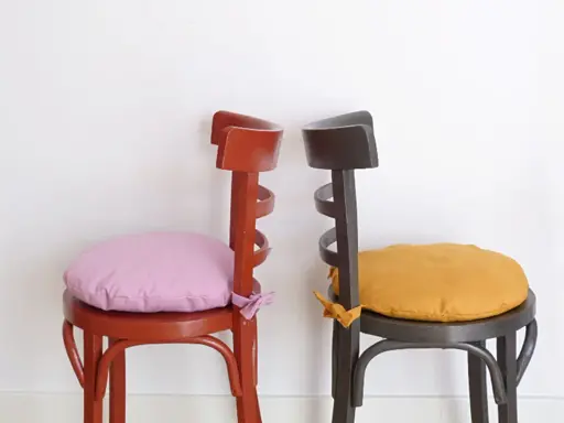 Dos sillas de madera pintadas, una roja con cojín lila y otra gris con cojín ocre. ¡Ideas para pintar sillas de madera!