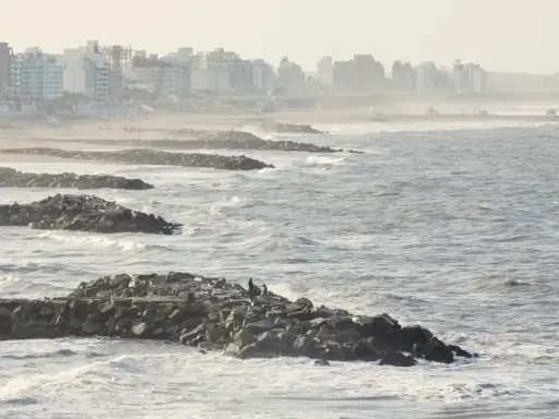 Olas rompen contra una escollera de rocas, protegiendo una ciudad costera. El escollera significado es claro: barrera contra el mar.