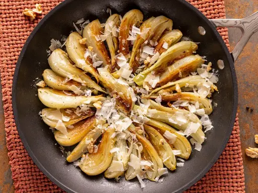 Finoçchi gratinati in padella, dorati e saporiti, guarniti con scaglie di formaggio e noci croccanti.