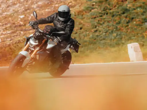 Motociclista con casco y chaqueta de cuero en una moto deportiva, disfrutando de la carretera. Ideal para quienes buscan el permiso conducir A1.