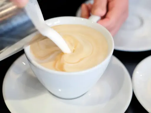 Milch wird in eine Tasse mit Kaffee gegossen, um ein cremiges Café au Lait zu kreieren.
