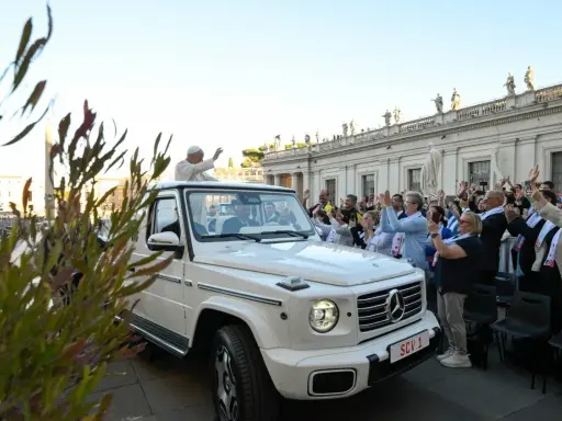 Papież Franciszek, mimo swojego vatican wiek, pozdrawia wiernych z białego mercedesa. Tłum wiwatuje, a niektórzy robią zdjęcia.