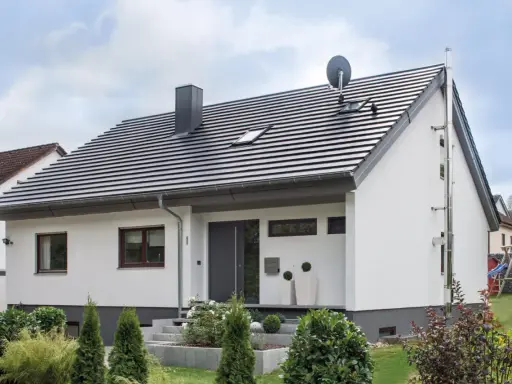 Nowoczesny dom z białymi ścianami i szarym dachem o kącie nachylenia dachu 30 stopni. Na dachu komin, anteny i okna dachowe.