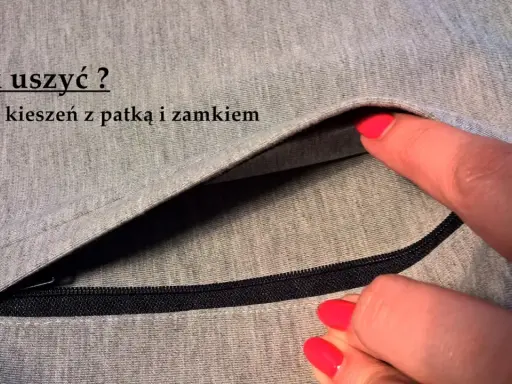 Szara tkanina z widocznym zamkiem i patką. Dłoń z czerwonym lakierem do paznokci wsuwa się do kieszeni z patką.