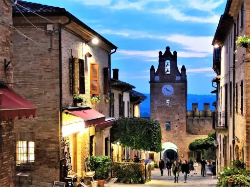 Serata magica al castello di Gradara. Vicoli illuminati, torre dell'orologio e gente che passeggia.