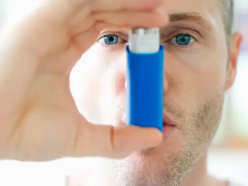 Mann mit blauen Augen hält einen blauen Inhalator, ein reliever asthma.