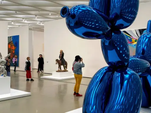 Visitors admire a giant blue balloon dog sculpture in a modern art gallery, a highlight among the top art galleries in the world.