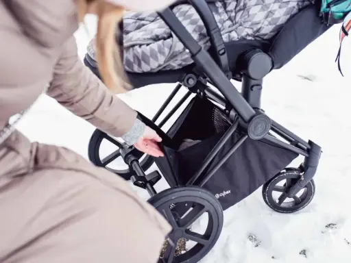 Kobieta wkłada coś do kosza wózka Cybex Priam. Waga wózka jest niewielka, co ułatwia manewrowanie w śniegu.