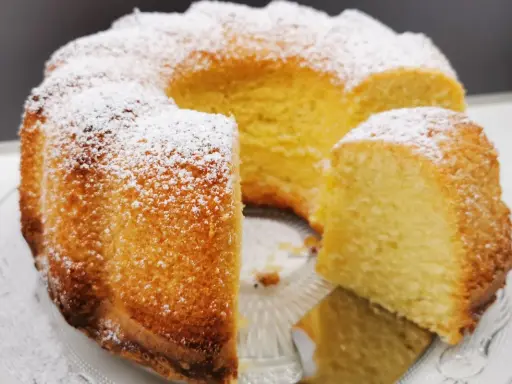 Wilgotna babka z ajerkoniakiem, oprószona cukrem pudrem, prezentuje się apetycznie na szklanej paterze.