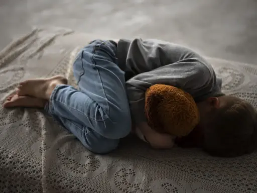 Un niño abraza un peluche, acurrucado en una cama. Una imagen que evoca la necesidad de saber como explicar la muerte a un niño.