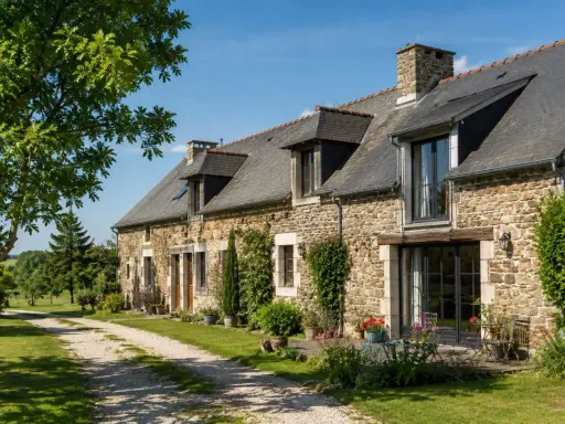 Longère moderne en pierre avec un chemin de gravier menant à l'entrée. Un jardin fleuri borde la façade.