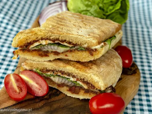 Pyszne panini z kurczakiem, suszonymi pomidorami i serem, podane z pomidorkami koktajlowymi i sałatą.