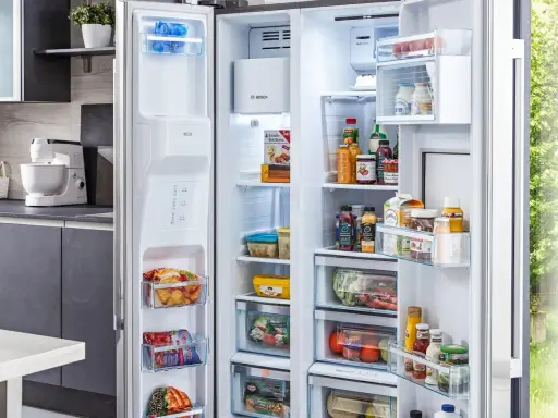 Offener Kühlschrank mit Lebensmitteln, darunter gefrorene Produkte und Getränke. Die Temperatur im Gefrierschrank ist ideal für die Lagerung.