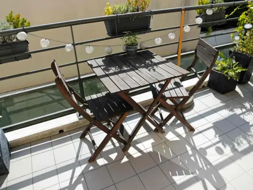 Un piccolo tavolo e sedie in legno su un balcone, con piante e lucine, perfetti per trasformare il balcone in terrazzo.