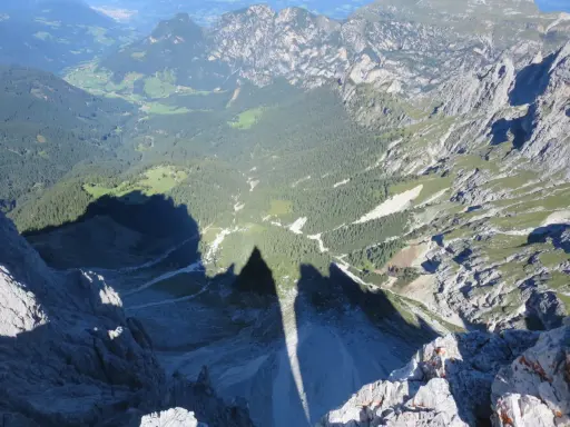 Ombra delle **Torri del Vajolet** che si allunga su un paesaggio alpino di boschi e valli verdi.