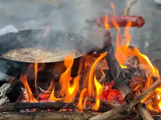 Matlagning över öppen eld, en härlig del av sportlov aktiviteter. Korv och mat i panna över flammande ved.