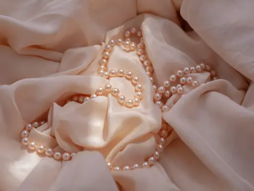 Un filo di perle rosa pallido adagiato su una morbida seta color crema. Un'idea perfetta per regalare perle.