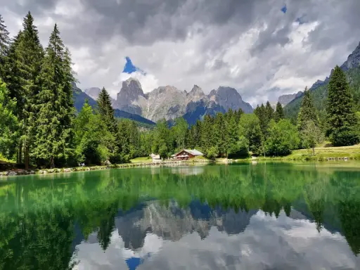 Riflessi perfetti sul lago Welsperg, con montagne maestose e una baita accogliente tra gli alberi.
