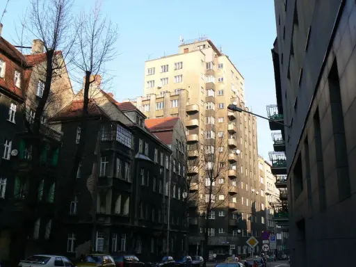 Wysoki, jasny drapacz chmur w Katowicach góruje nad starą kamienicą.
