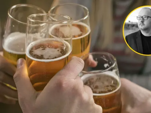 Ludzie wznoszą toasty piwem, podczas gdy w tle widać mężczyznę w okularach, który może symbolizować problem z alkoholem.