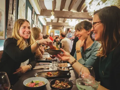Amies joyeuses partageant des tapas dans un resto ouvert le dimanche à Rennes. Ambiance chaleureuse et conviviale.