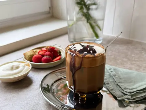 En läcker frappe med chokladsås och grädde, serverad med färska jordgubbar och en bit bakverk. Ett perfekt frappe recept för en solig dag.