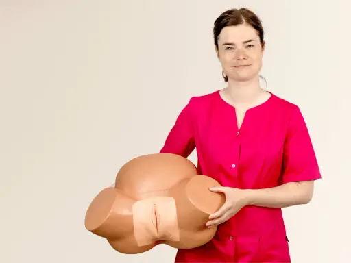 Kobieta w różowej bluzce trzyma model miednicy, demonstrując anatomię do nauki masażu szyjki macicy.