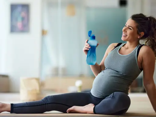 Donna incinta sorride con una bottiglia d'acqua dopo una sessione di yoga in gravidanza.