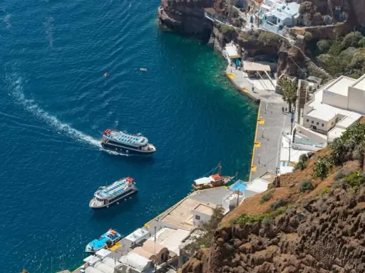 Barche turistiche navigano nel blu intenso del porto di Santorini, con le case bianche aggrappate alla scogliera.