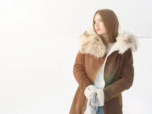 Mujer con abrigo de pelo natural en la nieve, lista para limpiar su ropa de invierno.