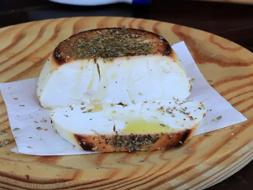 Ricotta al forno dorata e profumata con erbe aromatiche, servita su un tagliere di legno.
