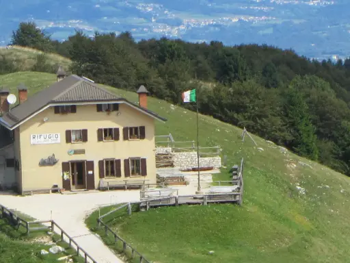 Il rifugio Posa Puner, con la bandiera italiana che sventola, domina un paesaggio montano verdeggiante.